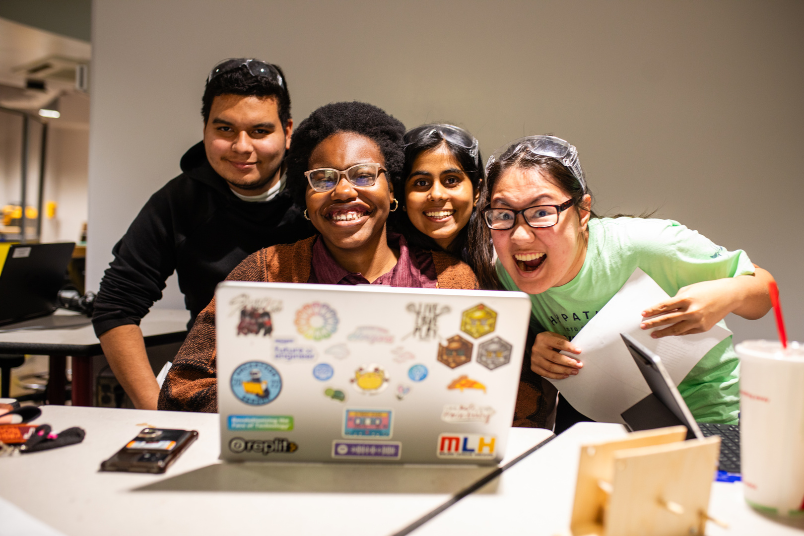 Four students posing for a photo in front of a laptop.