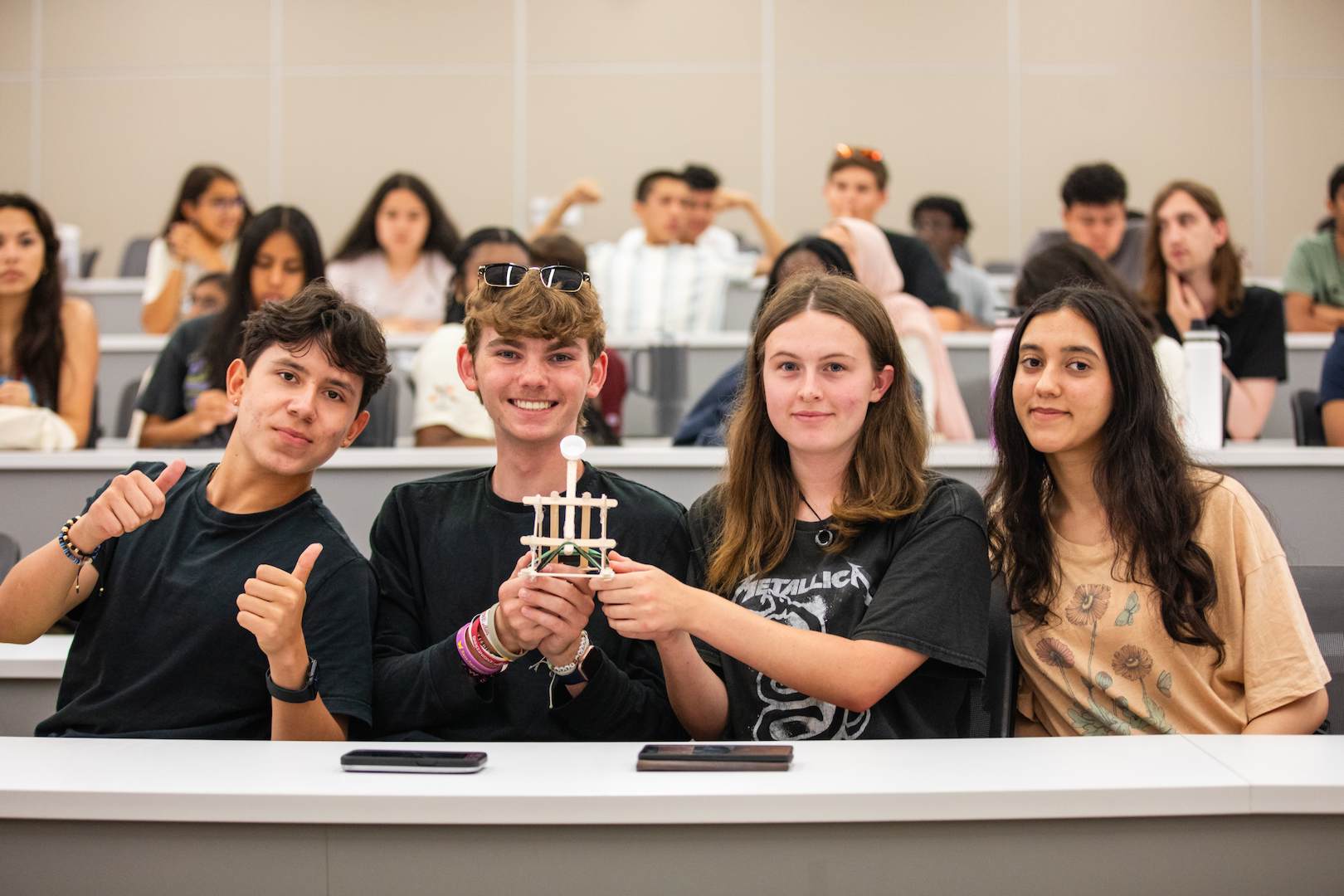 Four students in a classroom holding up their catapult
